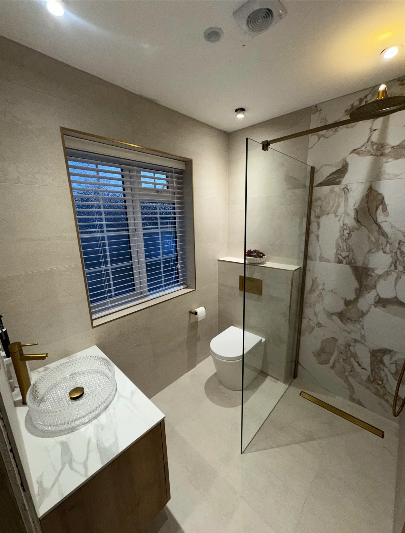 Elegant marble bathroom with clear glass walk-in shower, vessel basin, brass tap and window shutters — installed by Wokingham Bathroom Fitters in Wokingham, Berkshire