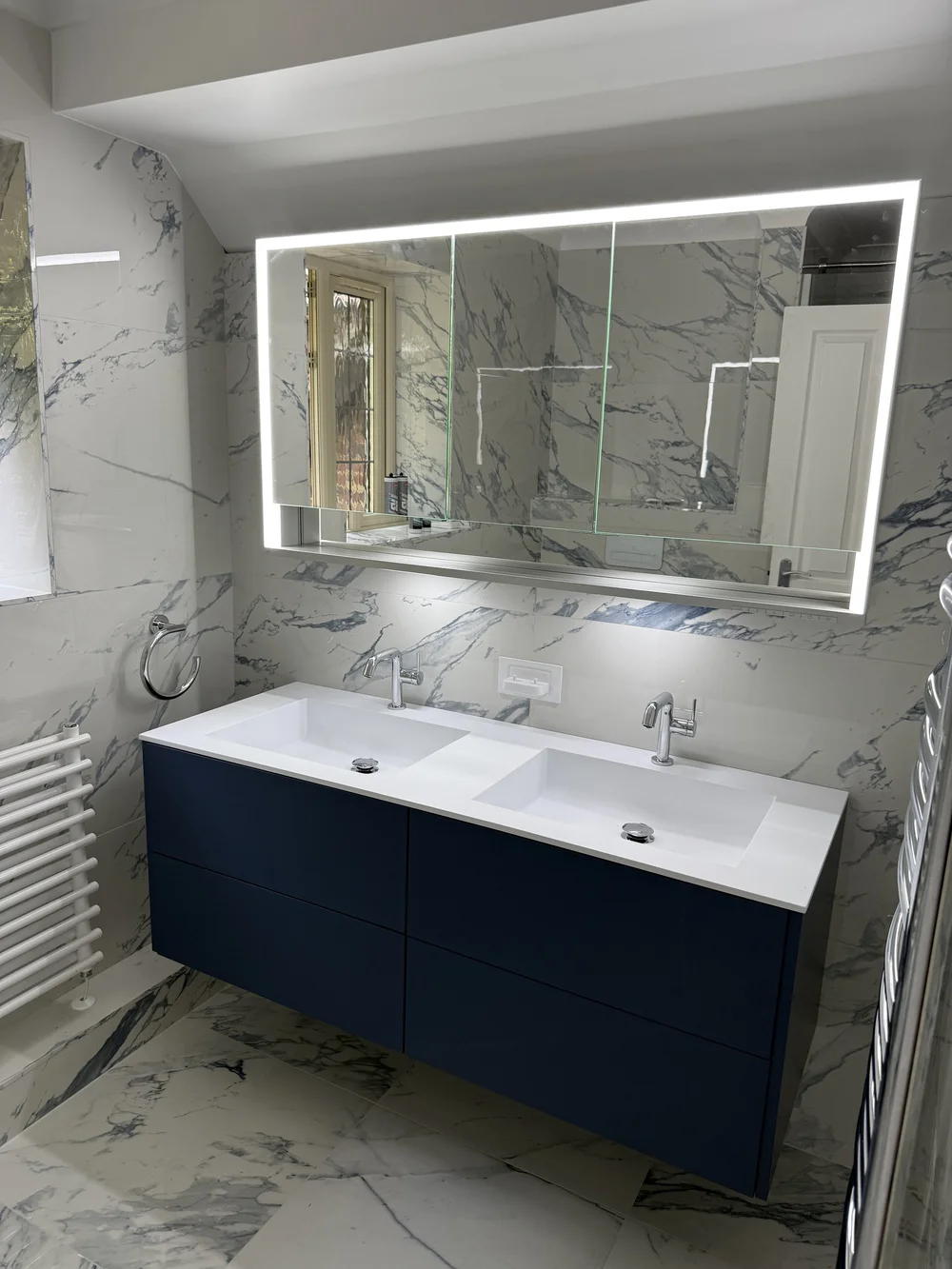 Navy vanity with marble walls and LED mirror — bathroom installation